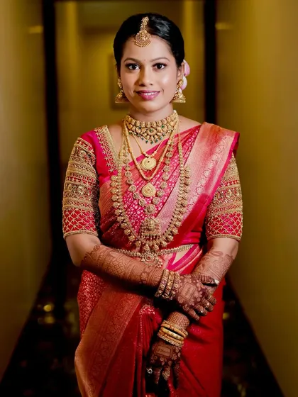 A full-length portrait of Lavanya, showcasing her complete bridal look with intricate gold jewelry and a radiant smile.