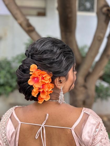 The same textured bun, now adorned with a bright orange floral accessory, showing how easily the look can be customized.