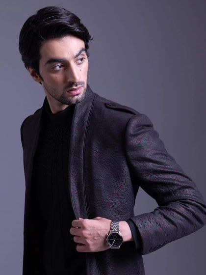 A jacket with a unique textured fabric and epaulets on the shoulders, paired with a black knit sweater for a sharp, modern look.