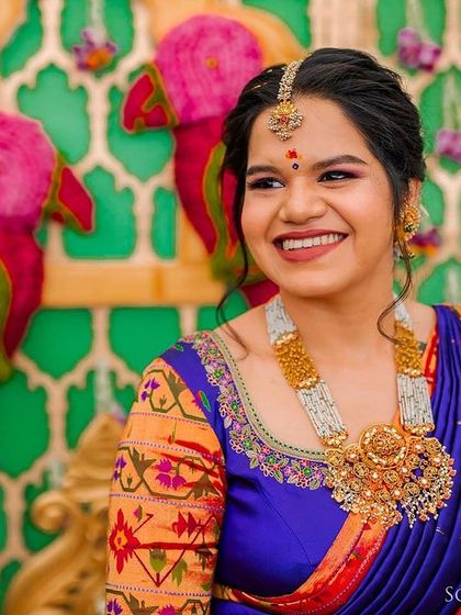 A joyful bride in a vibrant blue and orange saree, surrounded by colorful, traditional decor.
