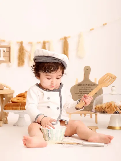 A baby dressed as a little chef pretends to mix ingredients in a bowl. This themed shoot is a creative way to capture a baby's playful spirit and curiosity.