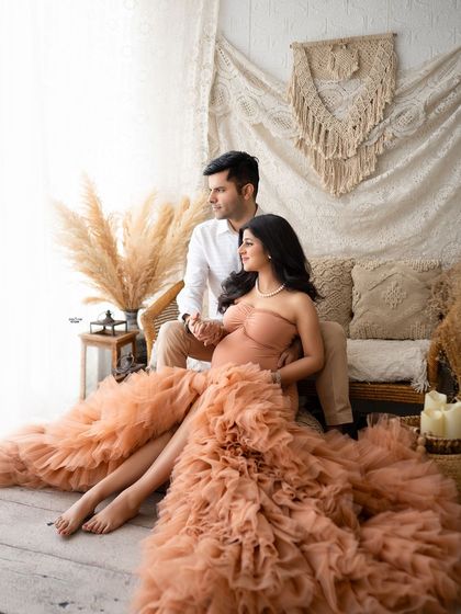 A wide shot of the couple, showing off the full, dramatic train of the peach gown against the cozy boho set.