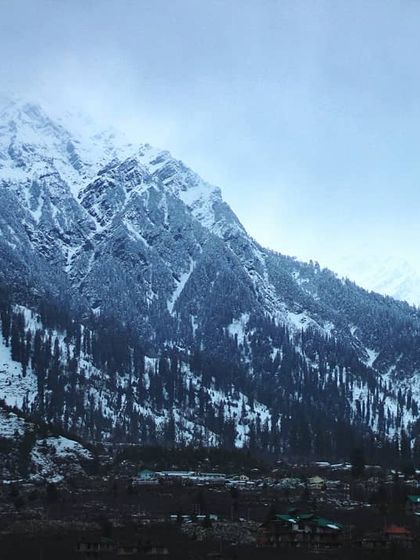 A wide view of a snow dusted mountain range in Himachal. The scene captures the cold, crisp air and the immense beauty of the landscape, a true definition of Himalayan happiness.