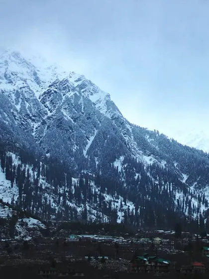 A wide view of a snow dusted mountain range in Himachal. The scene captures the cold, crisp air and the immense beauty of the landscape, a true definition of Himalayan happiness.