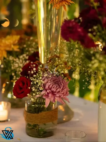 A close-up of a simple, rustic centerpiece. A glass jar wrapped in jute holds a small bouquet of red roses and baby's breath, showing that even small details can be thoughtfully designed.