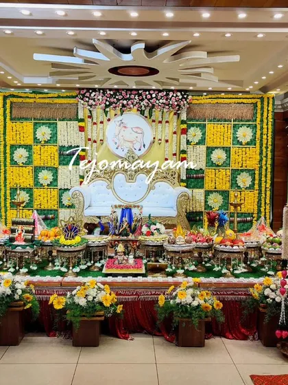 A baby shower setup with a yellow and green checkered backdrop and a floral arch. The stage is flanked by tall, decorated lamps.