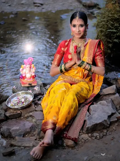 A full-length seated portrait by the water, showcasing the traditional drape of the Nauvari saree.