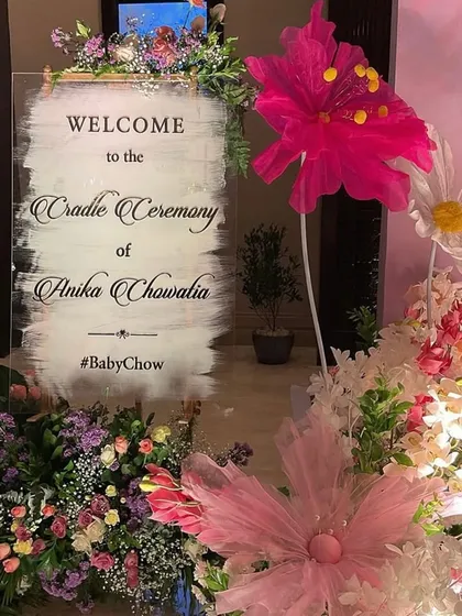 A personalized acrylic welcome sign for the cradle ceremony, surrounded by a lush arrangement of flowers. It's the first beautiful detail guests see.