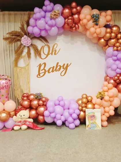 A fun and festive "Oh Baby" shower setup with a mix of colors and elements. The circular backdrop is framed by a balloon garland in purple, peach, and rose gold, with "Boy" and "Girl" foil balloons adding to the excitement.