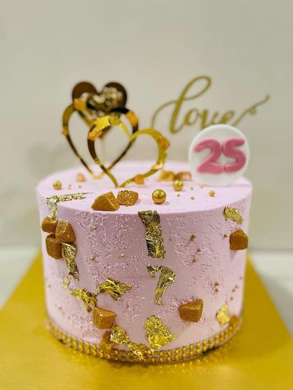 A lovely pink cake with gold leaf and butterscotch pieces, topped with golden hearts to celebrate a 25th milestone.
