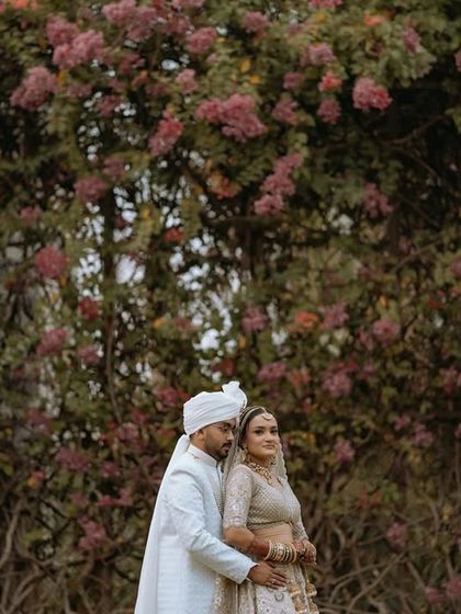 A wide, scenic portrait of the couple in their wedding attire against a beautiful backdrop of bougainvillea.