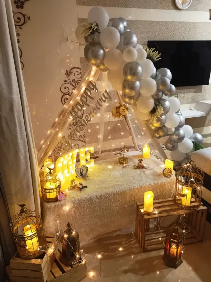 For a truly romantic anniversary, I can create an intimate cabana tent right in your home. This setup includes a plush rug, soft lighting from fairy lights and lanterns, and a beautiful silver and white balloon arch.