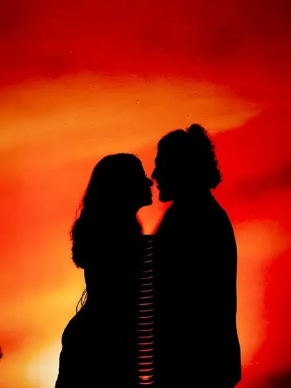 A festive silhouette against a fiery red and orange background, framed by Christmas trees. This shot has a warm, celebratory, and romantic holiday feel.