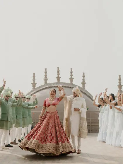 A grand celebration with the entire wedding party. The couple takes center stage, twirling happily as their bridesmaids and groomsmen cheer them on against a stunning architectural backdrop.