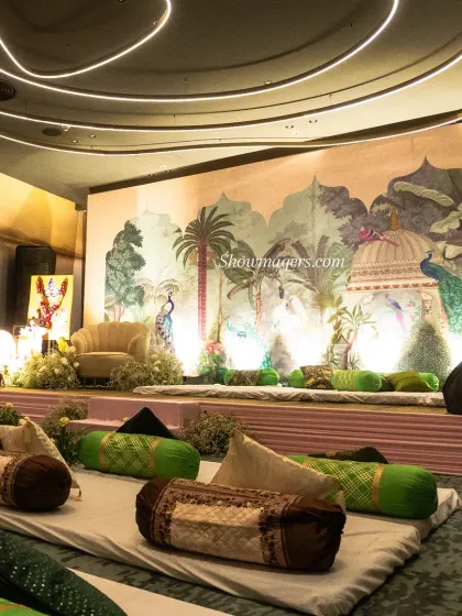 A low seating arrangement with traditional bolsters and a custom Pichwai art backdrop for the Mehendi ceremony, creating a relaxed yet elegant atmosphere.