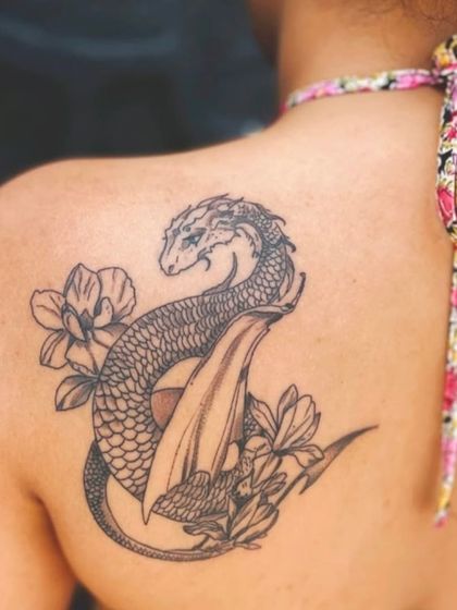 A snake and flower tattoo on the shoulder blade. This design combines the graceful curves of the snake with delicate floral elements for a balanced and artistic look.