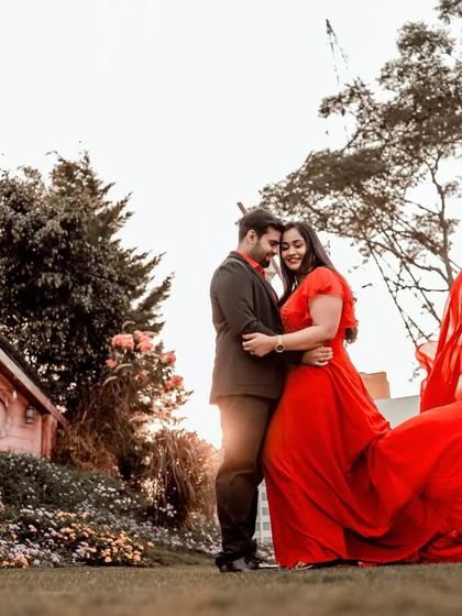 A fairytale-like pre-wedding photo with the bride in a stunning red dress with a long train, set in a whimsical garden.