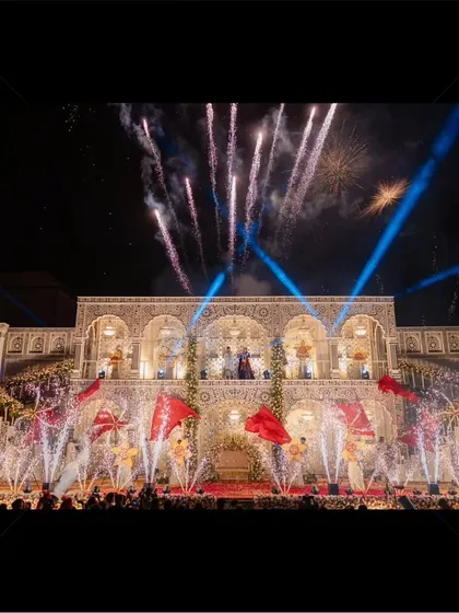 A wide shot showcasing the scale of a royal varmala production. You can see the massive stage, the crowd of guests, and the spectacular fireworks display that lights up the entire venue.