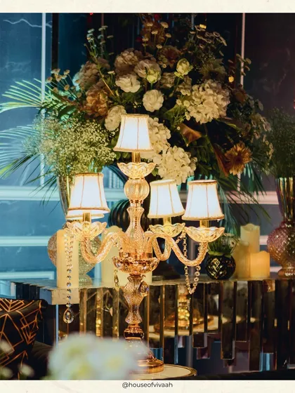 A close-up of a crystal candelabra with lampshades, set on a mirrored table, adding a touch of classic elegance to the modern, dramatic Sangeet decor.