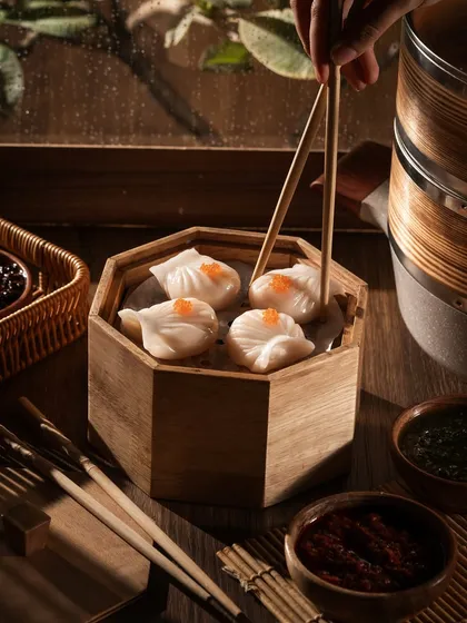 Using chopsticks to pick up a crystal shrimp dumpling (har gow). The lighting makes the translucent skin glow, showing the fresh filling inside.