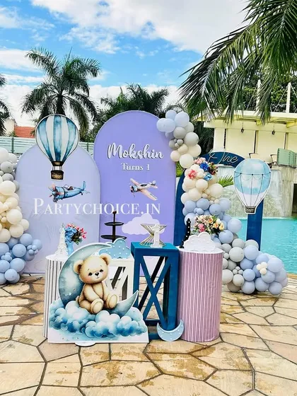 A stunning hot air balloon and teddy bear themed first birthday set up by a swimming pool. The pastel blue decor contrasts beautifully with the water.