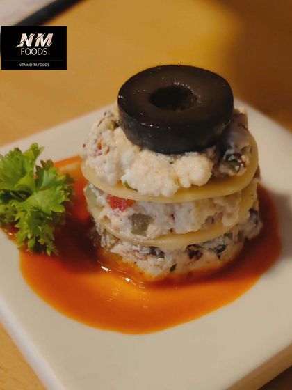 A mini lasagna stack, featuring layers of pasta, cheese, and sauce, topped with a black olive. This is a wonderful way to serve a classic Italian dish as a bite-sized appetizer.