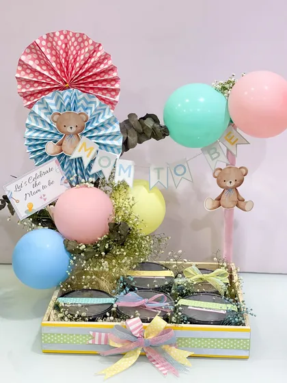 The full view of the baby shower food hamper, decorated with a "Mom to be" banner, teddy bears, and colorful balloons to create a celebratory atmosphere.