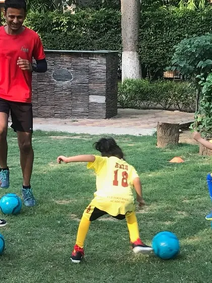 A coach leads a small group of our youngest players with blue balls. Football is a medium through which children learn life skills like resilience and discipline.