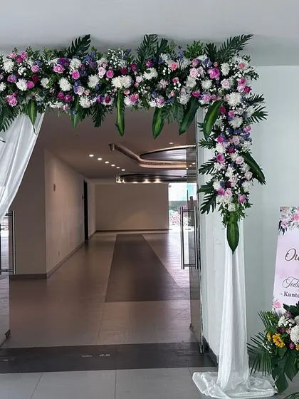 A lush floral entrance arch using a mix of white, pink, and purple flowers with tropical leaves, creating a grand welcome for guests.