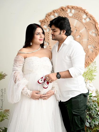 A romantic couple's portrait in the boho-floral setup. The tiny red shoes held by the dad-to-be are a sweet hint at the new life they are waiting for.