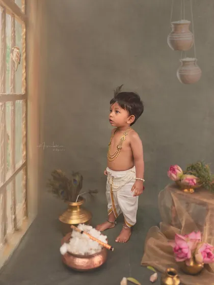 A full-body shot showing the complete styling, from the traditional dhoti and jewelry to the props that surround him. This is a classic pose for a baby Krishna photoshoot.