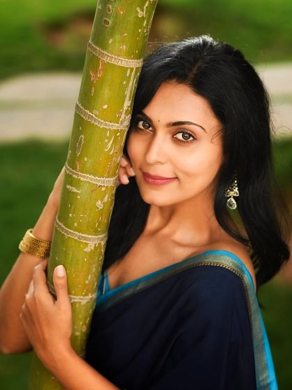 A close-up portrait with a natural element. Leaning against a bamboo stalk adds a unique, organic touch to this traditional saree look.