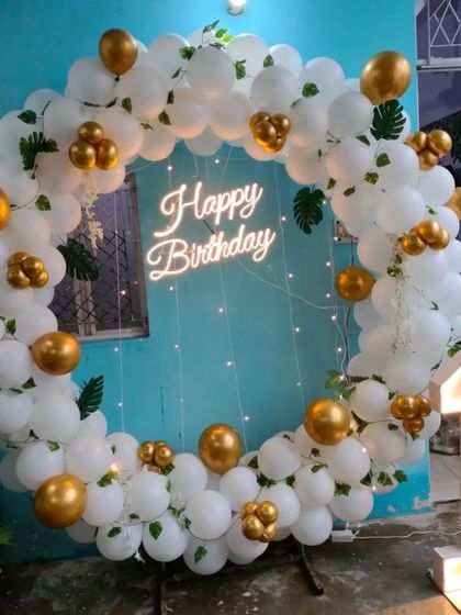An elegant white and gold theme for a first birthday. This decoration features a circular balloon arch with green leaf accents, a neon sign, and a light-up number '1', perfect for a classic celebration.