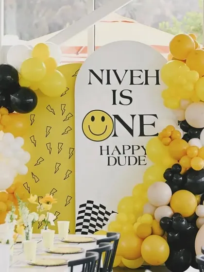 The backdrop for the sunshine-themed party, with a personalized 'Niveh is One' sign and a modern balloon garland in yellow, black, and white.
