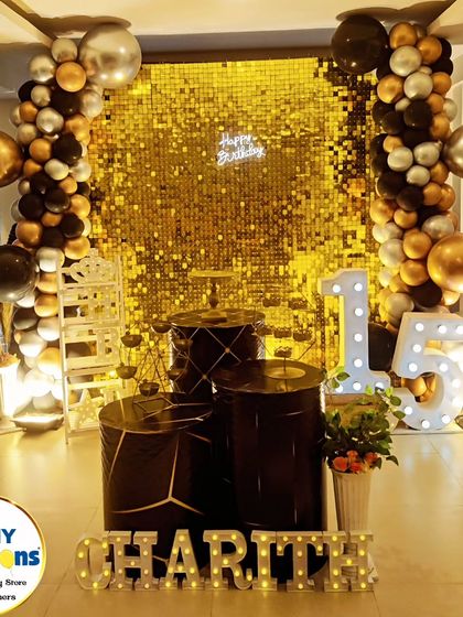 A chic and modern 15th birthday party. This setup uses a black and gold color scheme with a sequin wall, large marquee numbers, and geometric-patterned plinths.