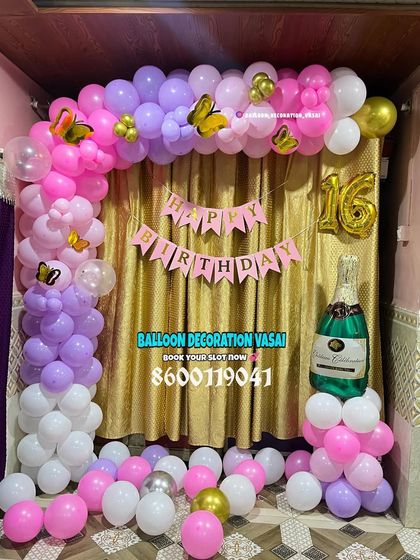 A sweet 16th birthday decoration. The balloon arch in purple, pink, and white is paired with a champagne bottle prop for a fun touch.