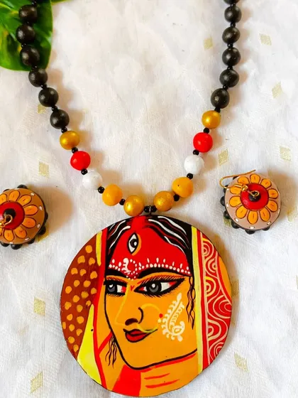 I pour my heart and devotion into these hand-painted pendants. This piece features the serene face of a goddess, detailed with traditional motifs, making it perfect for festive occasions or as a piece of wearable art. The necklace is strung with terracotta beads that complement the pendant.