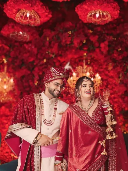 A happy, candid shot of the couple after their jaimala ceremony, surrounded by a magnificent wall of red flowers. Their smiles say it all.