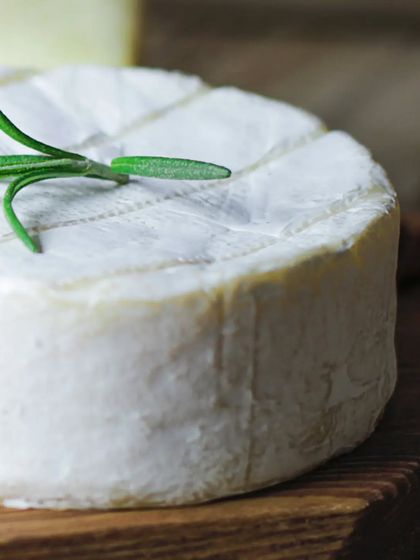 A beautiful close-up of a wheel of soft, creamy cheese, topped with a sprig of fresh rosemary. This shot is all about highlighting the quality of the artisanal cheese I source.