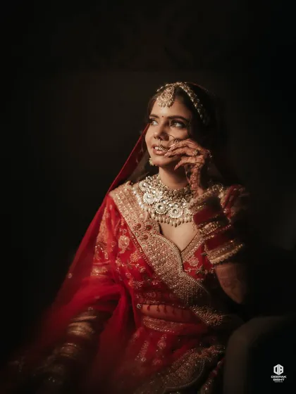 A dreamy, artistic shot capturing the shyness and beauty of the bride. The focus here is on the soft glam and the traditional red veil.