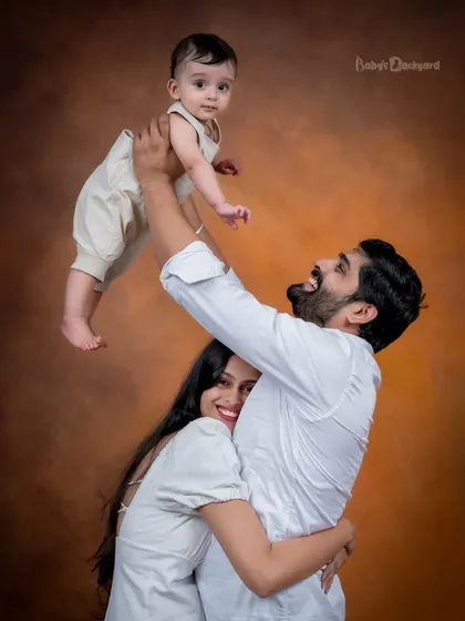 Lifting their little one high, this family is full of joy and laughter. The warm studio background adds a beautiful glow to this happy family picture.