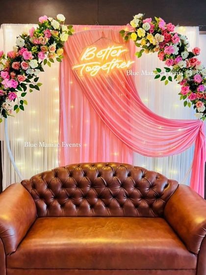 A lovely Roka backdrop with a circular frame, pink draping, and a pink and white floral arch. The tufted leather sofa adds a touch of classic comfort to the modern setup.