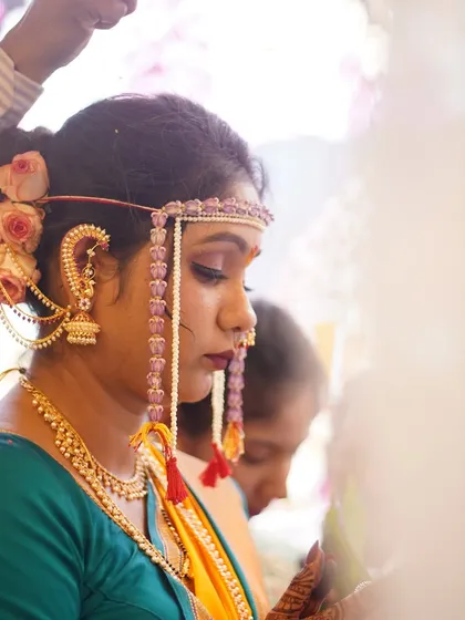 A side view showing the intricate Khopa hairstyle adorned with fresh pink roses, complementing the bride's traditional jewellery.