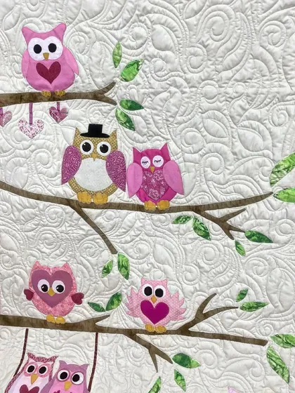 An adorable owl-themed baby quilt, with a family of pink owls sitting on tree branches.