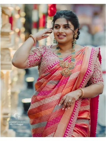 Varsha looking radiant in a vibrant pink and orange saree. The soft, romantic hairstyle with face-framing tendrils perfectly complements the traditional yet modern feel of her outfit.