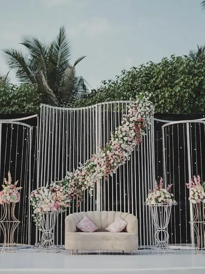 A modern and elegant reception stage. The clean lines of the white panelled backdrop are softened by asymmetrical cascades of pink and white flowers, creating a chic and sophisticated look.