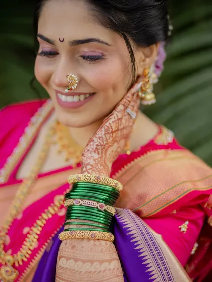 A candid moment of happiness. The focus is on the bride's glowing smile, the intricate henna, and the traditional green glass bangles, essential elements of a Maharashtrian bride's attire.