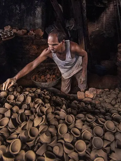 A potter carefully inspects a fresh batch of diyas, or clay lamps, before they are fired. The sheer volume of his craft fills the frame, showing the scale of production in this small workshop.