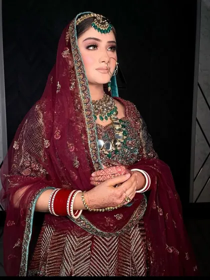 A stunning bride in a deep maroon lehenga, wearing a heavy emerald and polki set. The color combination is rich and luxurious.