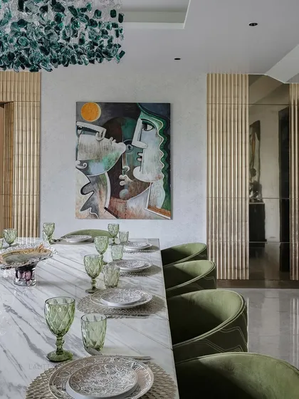 A closer look at the artful composition of the dining area. The abstract painting on the wall complements the green velvet chairs and the unique, sculptural chandelier made of green glass.